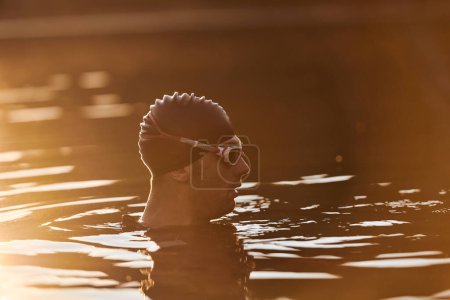 Téléchargez les photos : Un triathlète trouve un rajeunissement serein dans un lac, se prélassant dans la tranquillité de l'eau après une séance d'entraînement intense. - en image libre de droit