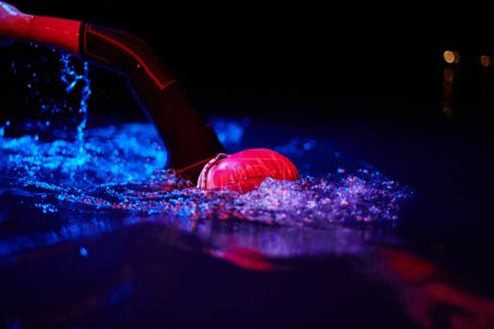 Téléchargez les photos : Vrai nageur triathlète ayant une pause pendant l'entraînement dur au lac sur les lumières de couleur de gel de néon de nuit sombre - en image libre de droit