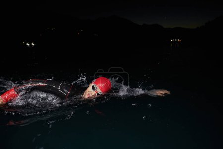 Téléchargez les photos : Un triathlète professionnel déterminé subit un entraînement nocturne rigoureux dans les eaux froides, faisant preuve de dévouement et de résilience en préparation d'une prochaine compétition de natation de triathlon. - en image libre de droit