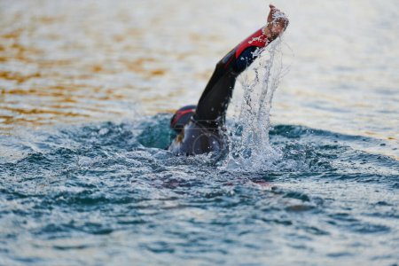 Téléchargez les photos : Athlète de triathlon nageant sur le lac au lever du soleil portant une combinaison. Photo de haute qualité - en image libre de droit