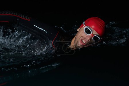 Foto de Un determinado triatleta profesional se somete a un riguroso entrenamiento nocturno en aguas frías, mostrando dedicación y resiliencia en preparación para una próxima competición de natación de triatlón.. - Imagen libre de derechos