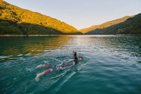Foto de Atleta de triatlón nadando en el lago al amanecer usando traje de neopreno. Foto de alta calidad - Imagen libre de derechos