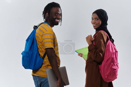 Foto de Estudiante afroamericano colabora con su colega musulmán, quien trabaja diligentemente en su computadora portátil, simbolizando una mezcla de diversidad, aprendizaje moderno y espíritu cooperativo contra un blanco sereno - Imagen libre de derechos