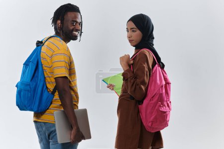 Foto de Estudiante afroamericano colabora con su colega musulmán, quien trabaja diligentemente en su computadora portátil, simbolizando una mezcla de diversidad, aprendizaje moderno y espíritu cooperativo contra un blanco sereno - Imagen libre de derechos