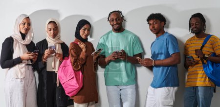 Foto de Un grupo diverso de estudiantes, inmersos en la era digital, se mantiene unido mientras se relacionan con sus teléfonos inteligentes en un contexto blanco, que simboliza la era moderna de la conectividad, la comunicación y - Imagen libre de derechos