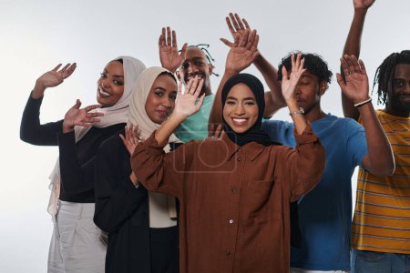 Téléchargez les photos : Un groupe jubilatoire et diversifié, dont un homme afro-américain et des filles portant le hijab, saluent et célèbrent avec exubérance, incarnant le dynamisme de la vie étudiante dans un contexte blanc, symbolisant - en image libre de droit