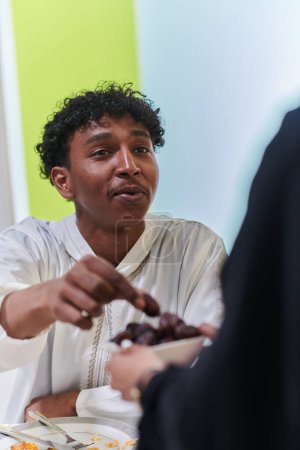 Téléchargez les photos : L'homme musulman afro-américain prend délicatement rendez-vous pour rompre son jeûne pendant le mois du Ramadan, assis à la table du dîner familial, incarnant une scène de réflexion spirituelle, de tradition culturelle et de - en image libre de droit