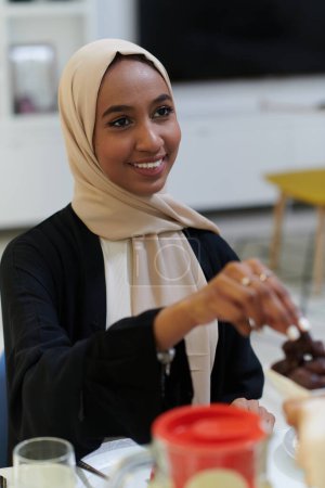 Foto de Una joven musulmana adornada con un hiyab delicadamente toma dátiles, simbolizando la ruptura de su ayuno en el mes santo del Ramadán, encapsulando una escena de reflexión espiritual, tradición cultural, y - Imagen libre de derechos