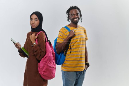 Téléchargez les photos : Dans un contexte blanc pur, deux étudiants, un jeune homme afro-américain et une femme portant le hijab, utilisent des ordinateurs portables en collaboration dans une démonstration d'autonomisation technologique et d'éducation inclusive. - en image libre de droit