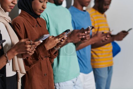 Foto de Un grupo diverso de estudiantes, inmersos en la era digital, se mantiene unido mientras se relacionan con sus teléfonos inteligentes en un contexto blanco, que simboliza la era moderna de la conectividad, la comunicación y - Imagen libre de derechos