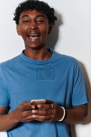 Téléchargez les photos : L'adolescent afro-américain s'engage avec son smartphone sur un fond blanc immaculé, résumant l'essence de la connectivité numérique contemporaine et de la culture de la jeunesse. - en image libre de droit