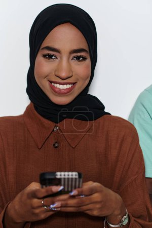 Photo for An elegant Arab woman, adorned in a hijab, engages with modernity as she uses a smartphone, the juxtaposition of traditional attire against contemporary technology captured in the isolated setting - Royalty Free Image