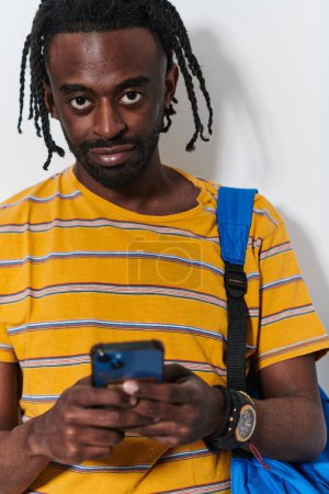 Téléchargez les photos : L'adolescent afro-américain s'engage avec son smartphone sur un fond blanc immaculé, résumant l'essence de la connectivité numérique contemporaine et de la culture de la jeunesse. - en image libre de droit