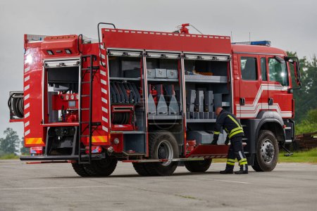 Téléchargez les photos : Un pompier prépare méticuleusement un camion de pompiers moderne pour une mission d'évacuation et d'intervention en cas de situations dangereuses, faisant preuve du plus grand dévouement à la sécurité et à la préparation face à un incendie - en image libre de droit