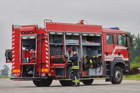 Foto de Un bombero prepara meticulosamente un camión de bomberos moderno para una misión de evacuación y respuesta a situaciones peligrosas, mostrando la máxima dedicación a la seguridad y preparación frente a un incendio - Imagen libre de derechos