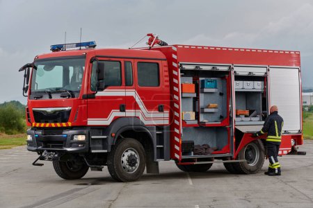 Foto de Un bombero prepara meticulosamente un camión de bomberos moderno para una misión de evacuación y respuesta a situaciones peligrosas, mostrando la máxima dedicación a la seguridad y preparación frente a un incendio - Imagen libre de derechos