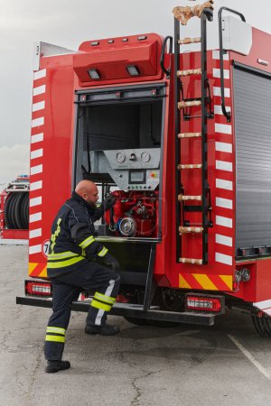 Téléchargez les photos : Un pompier prépare méticuleusement un camion de pompiers moderne pour une mission d'évacuation et d'intervention en cas de situations dangereuses, faisant preuve du plus grand dévouement à la sécurité et à la préparation face à un incendie - en image libre de droit