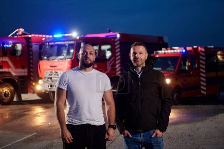 Photo for Group of firefighters, dressed in civilian clothing, stand in front of fire trucks during the night, showcasing a moment of camaraderie and unity among the team as they reflect on their duties and the - Royalty Free Image