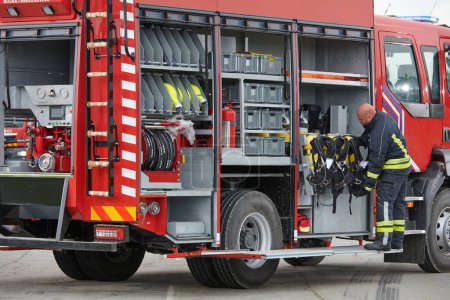 Photo for A firefighter meticulously prepares a modern firetruck for a mission to evacuate and respond to dangerous situations, showcasing the utmost dedication to safety and readiness in the face of a fire - Royalty Free Image