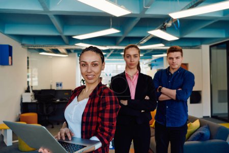 Photo for A young team of business professionals poses for a startup office portrait, exuding confidence and ambition, with one woman holding a laptop, symbolizing innovation and collaboration in - Royalty Free Image