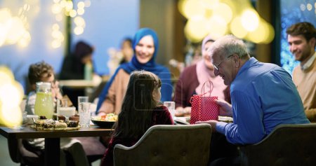 Photo for Grandparents arrive at their childrens and grandchildrens gathering for iftar in a restaurant during the holy month of Ramadan, bearing gifts and sharing cherished moments of love, unity, and - Royalty Free Image