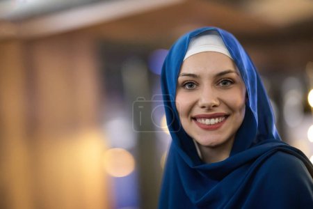 Foto de En un restaurante moderno, una hermosa mujer musulmana europea disfruta con gracia del ambiente y las delicias culinarias durante el mes santo del Ramadán, encarnando la elegancia y la serenidad espiritual en medio de - Imagen libre de derechos