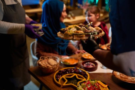 Foto de En una escena conmovedora, un chef profesional sirve a una familia musulmana europea su comida iftar durante el mes sagrado del Ramadán, encarnando la unidad cultural y la hospitalidad culinaria en un momento de compartir - Imagen libre de derechos