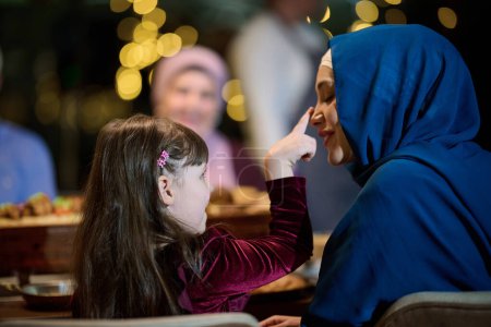 In einer herzerwärmenden Szene lassen sich eine glückliche islamische europäische Familie und ein junges Mädchen reizvoll auf ihre Mutter ein, während sie ihrem Iftar-Essen entgegenfiebern und Freude, Liebe und familiäre Bindung ausstrahlen.