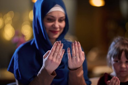 In a modern restaurant, a beautiful hijab-wearing woman prays with her hands raised, epitomizing grace, serenity, and spiritual devotion. 