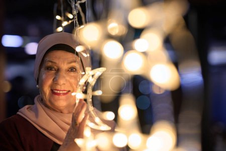 In einem modernen Restaurant-Ambiente macht eine Frau im Hijab ein Selfie neben leuchtenden Lichtern und präsentiert zeitgenössischen Stil und kulturelle Vielfalt in einer trendigen urbanen Umgebung. 