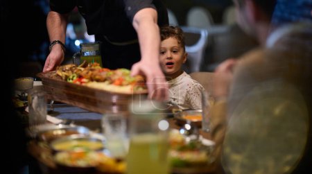 Foto de En una escena conmovedora, un chef profesional sirve a una familia musulmana europea su comida iftar durante el mes sagrado del Ramadán, encarnando la unidad cultural y la hospitalidad culinaria en un momento de compartir - Imagen libre de derechos