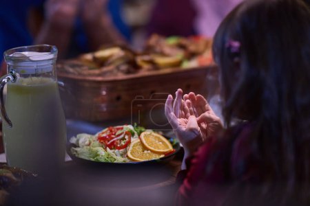 Photo for A young girl raises her hands in prayer as she prepares for her iftar meal during the holy month of Ramadan, embodying spiritual devotion and innocence - Royalty Free Image