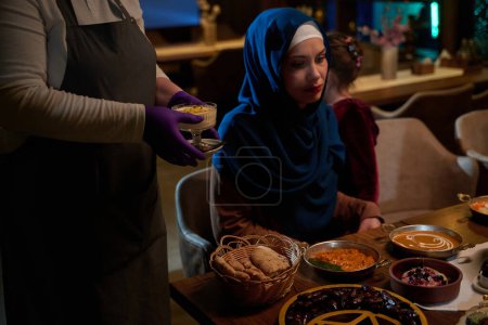 Dans une scène chaleureuse, un chef professionnel sert à une famille musulmane européenne son repas iftar pendant le mois sacré du Ramadan, incarnant l'unité culturelle et l'hospitalité culinaire dans un moment de partage