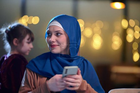 Una hermosa mujer musulmana europea, adornada con un hiyab, utiliza su teléfono inteligente para prepararse rápidamente para iftar durante el sagrado mes de Ramadán, encarnando la mezcla de tradición y modernidad en su