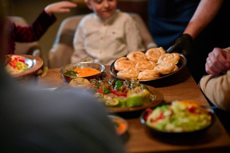 Dans une scène chaleureuse, un chef professionnel sert à une famille musulmane européenne son repas iftar pendant le mois sacré du Ramadan, incarnant l'unité culturelle et l'hospitalité culinaire dans un moment de partage