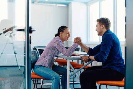 Photo for In a modern startup office, a businessman and a businesswoman business colleagues engage in a symbolic arm-wrestling match, reflecting teamwork, competition, and innovation in their dynamic workplace - Royalty Free Image