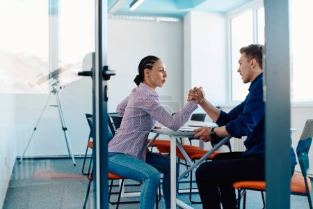 Photo for In a modern startup office, a businessman and a businesswoman business colleagues engage in a symbolic arm-wrestling match, reflecting teamwork, competition, and innovation in their dynamic workplace - Royalty Free Image