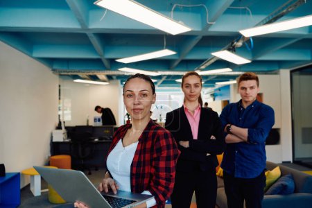 Photo for A young team of business professionals poses for a startup office portrait, exuding confidence and ambition, with one woman holding a laptop, symbolizing innovation and collaboration in - Royalty Free Image