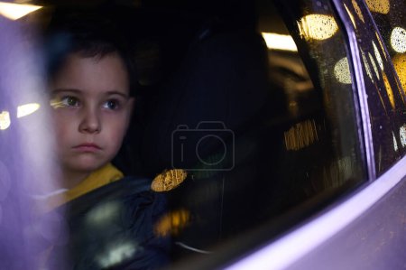 Téléchargez les photos : Un jeune garçon profite d'une promenade en voiture, capturé par la fenêtre, comme il observe le paysage de passage - en image libre de droit