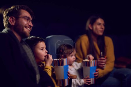 Eine moderne Familie genießt die gemeinsame Zeit im Kino und gönnt sich Popcorn, während sie mit ihren Kindern einen Film schaut.