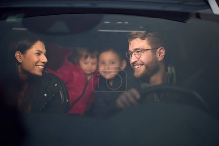 En las horas nocturnas, una familia feliz disfruta de momentos lúdicos juntos dentro de un coche mientras viajan en un viaje nocturno por carretera, iluminados por el resplandor de los faros y llenos de risa y alegría.