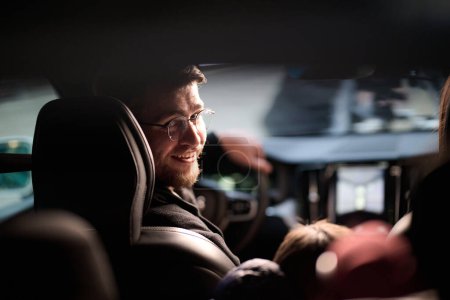Téléchargez les photos : Dans les heures nocturnes, une famille heureuse profite de moments ludiques ensemble à l'intérieur d'une voiture alors qu'ils voyagent sur une route nocturne, éclairés par la lueur des phares et remplis de rire et de joie. - en image libre de droit