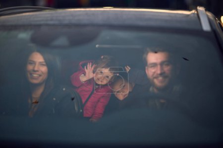 Foto de En las horas nocturnas, una familia feliz disfruta de momentos lúdicos juntos dentro de un coche mientras viajan en un viaje nocturno por carretera, iluminados por el resplandor de los faros y llenos de risa y alegría. - Imagen libre de derechos