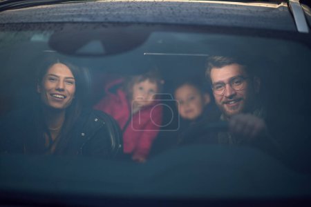 En las horas nocturnas, una familia feliz disfruta de momentos lúdicos juntos dentro de un coche mientras viajan en un viaje nocturno por carretera, iluminados por el resplandor de los faros y llenos de risa y alegría.