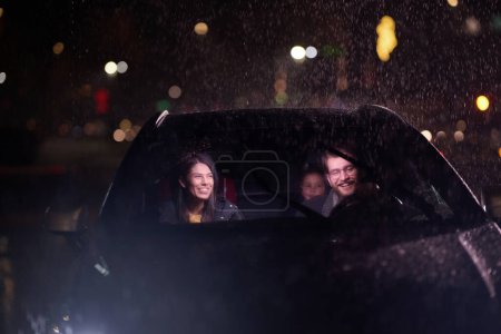 En medio de un viaje nocturno, una familia feliz disfruta de momentos lúdicos dentro de un automóvil mientras viajan a través del tiempo lluvioso, iluminados por el resplandor de los faros, la risa y la unión.