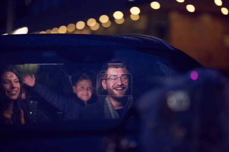 Téléchargez les photos : Dans les heures nocturnes, une famille heureuse profite de moments ludiques ensemble à l'intérieur d'une voiture alors qu'ils voyagent sur une route nocturne, éclairés par la lueur des phares et remplis de rire et de joie. - en image libre de droit