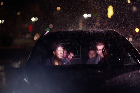 Au milieu d'un voyage nocturne, une famille heureuse profite de moments ludiques à l'intérieur d'une voiture alors qu'ils voyagent par temps pluvieux, illuminés par la lueur des phares, des rires et des liens.