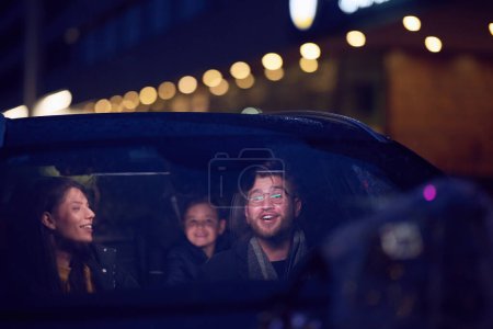 In the nighttime hours, a happy family enjoys playful moments together inside a car as they journey on a nocturnal road trip, illuminated by the glow of headlights and filled with laughter and joy.