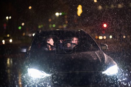 Foto de En medio de un viaje nocturno, una familia feliz disfruta de momentos lúdicos dentro de un automóvil mientras viajan a través del tiempo lluvioso, iluminados por el resplandor de los faros, la risa y la unión. - Imagen libre de derechos