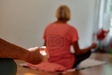 In diesem sonnenbeschienenen Raum nimmt eine ältere Frauenhand anmutig verschiedene Yoga-Posen ein und verkörpert die Essenz aktiven Alterns, Gesundheit und inneren Friedens.. 